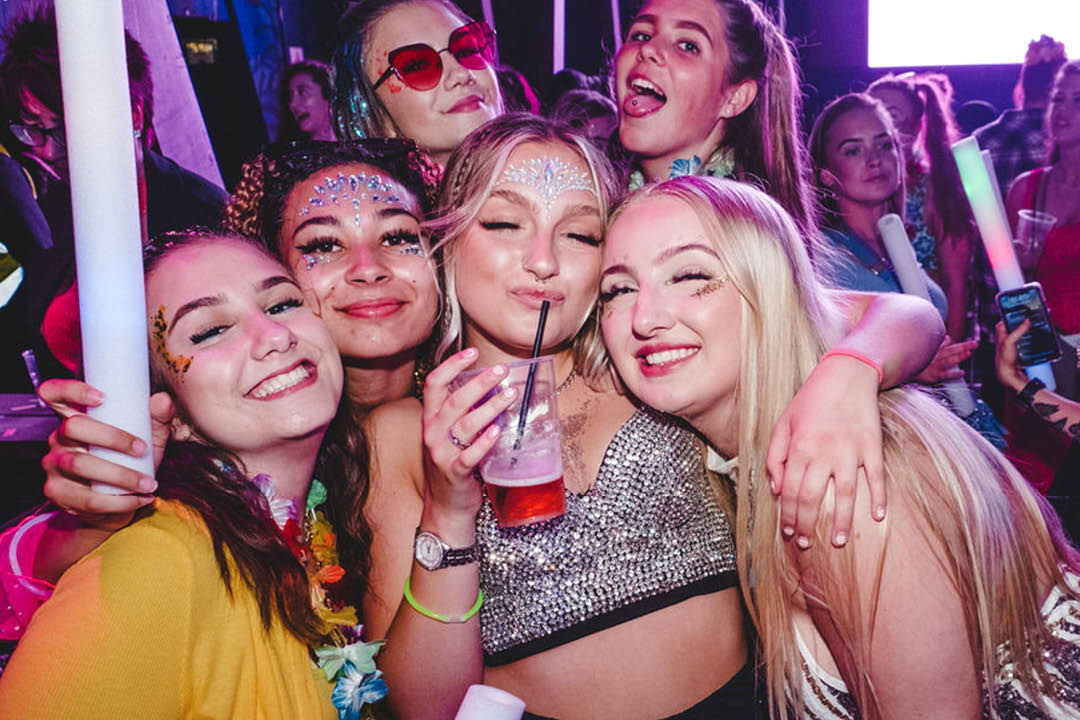 A group of friends hugging and posing in sparkly outfits and glitter at Glitterfest